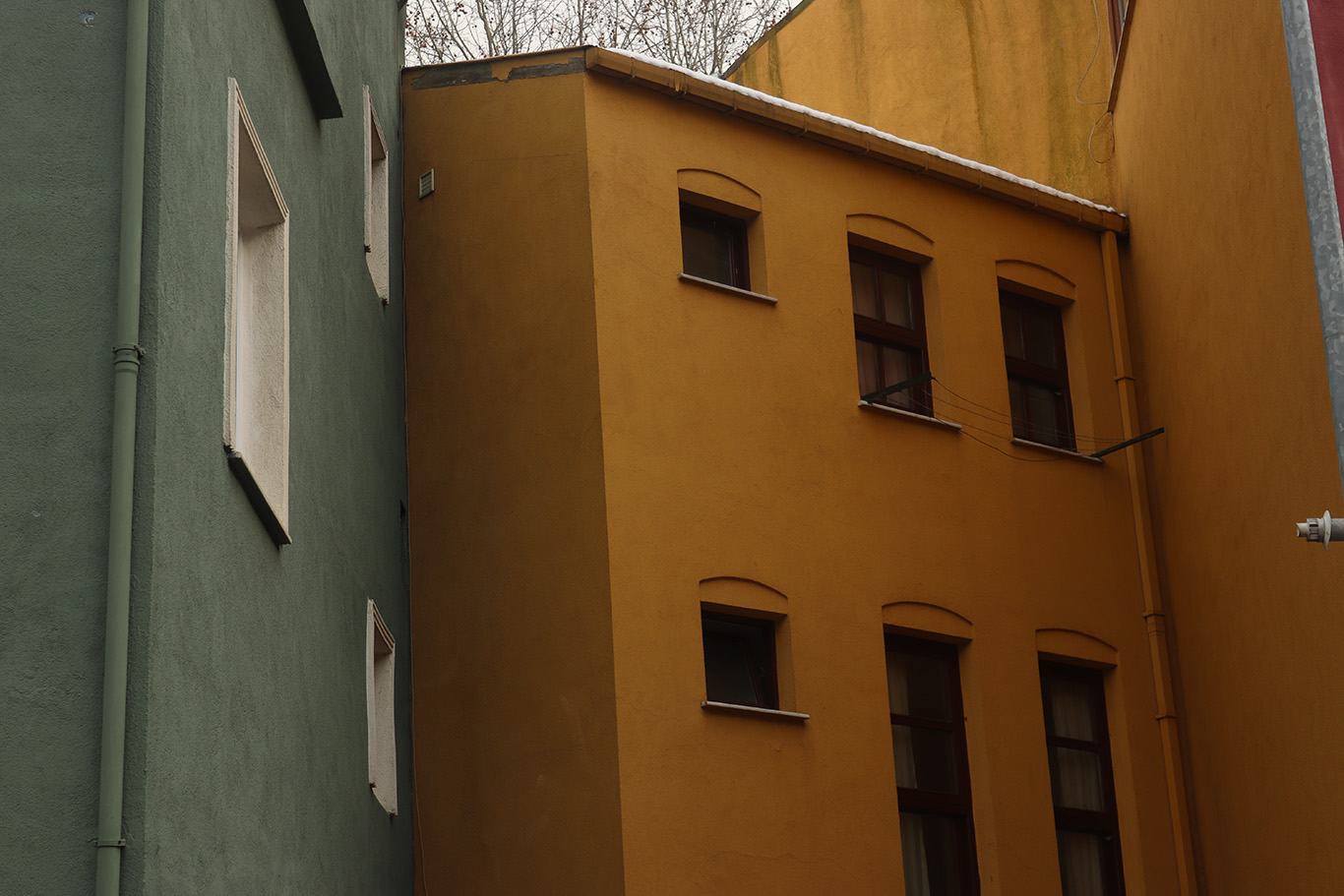 A dark yellow building standing next to a pastel green building in a street corner.