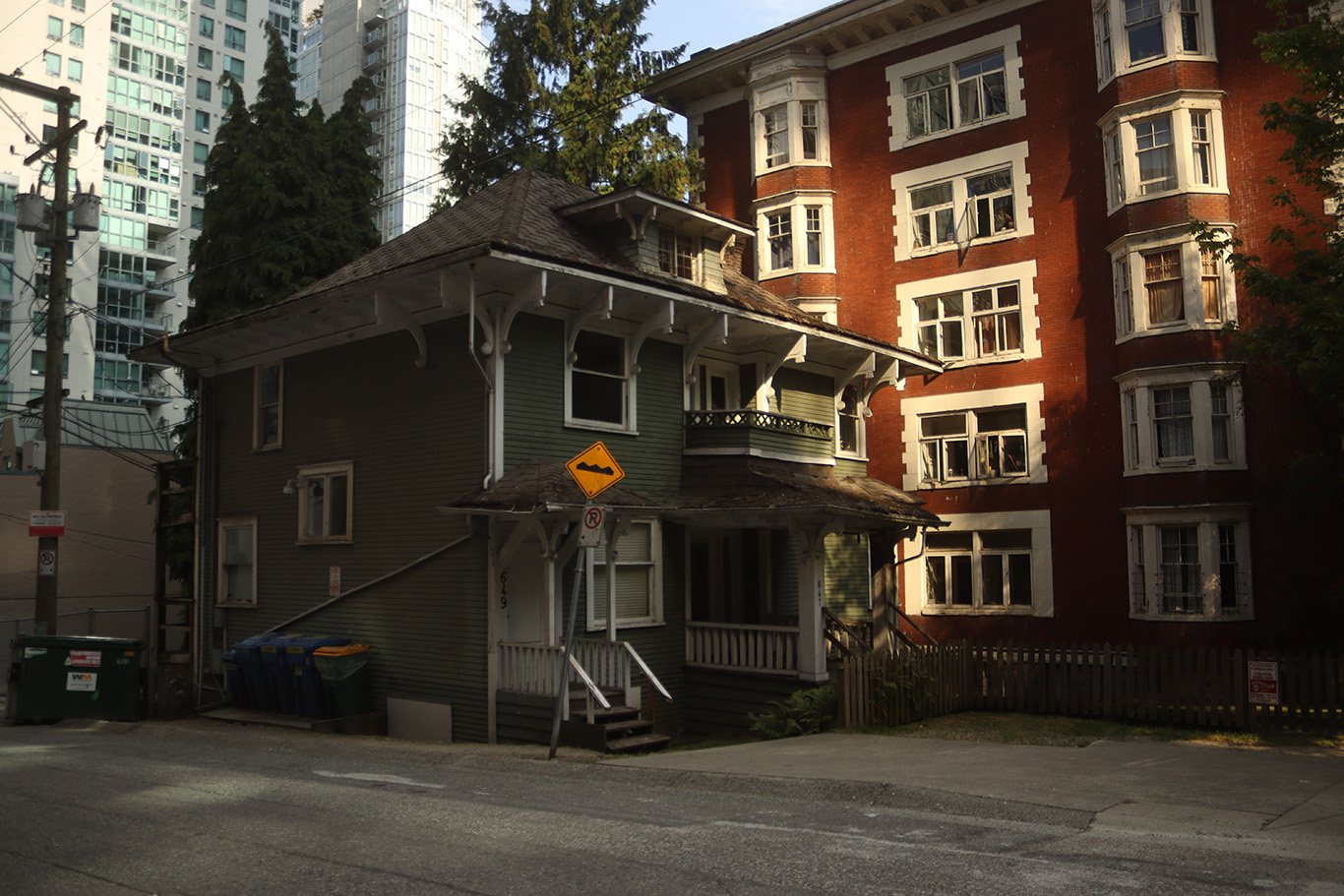 A green two storey house next to a brick red five storey apartment building.