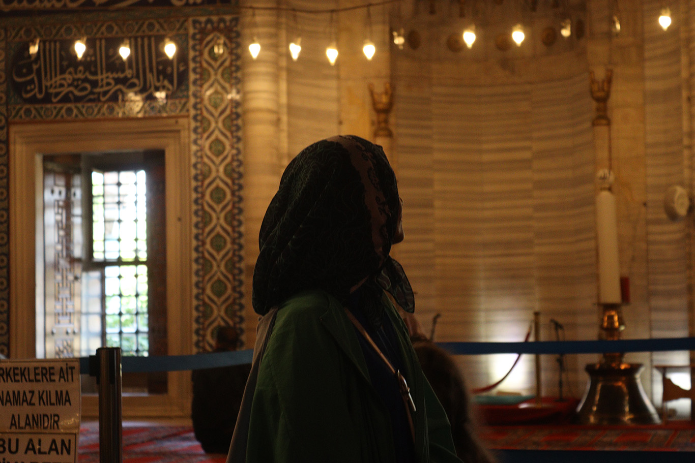 A woman standing in a mosque under warm string lights.